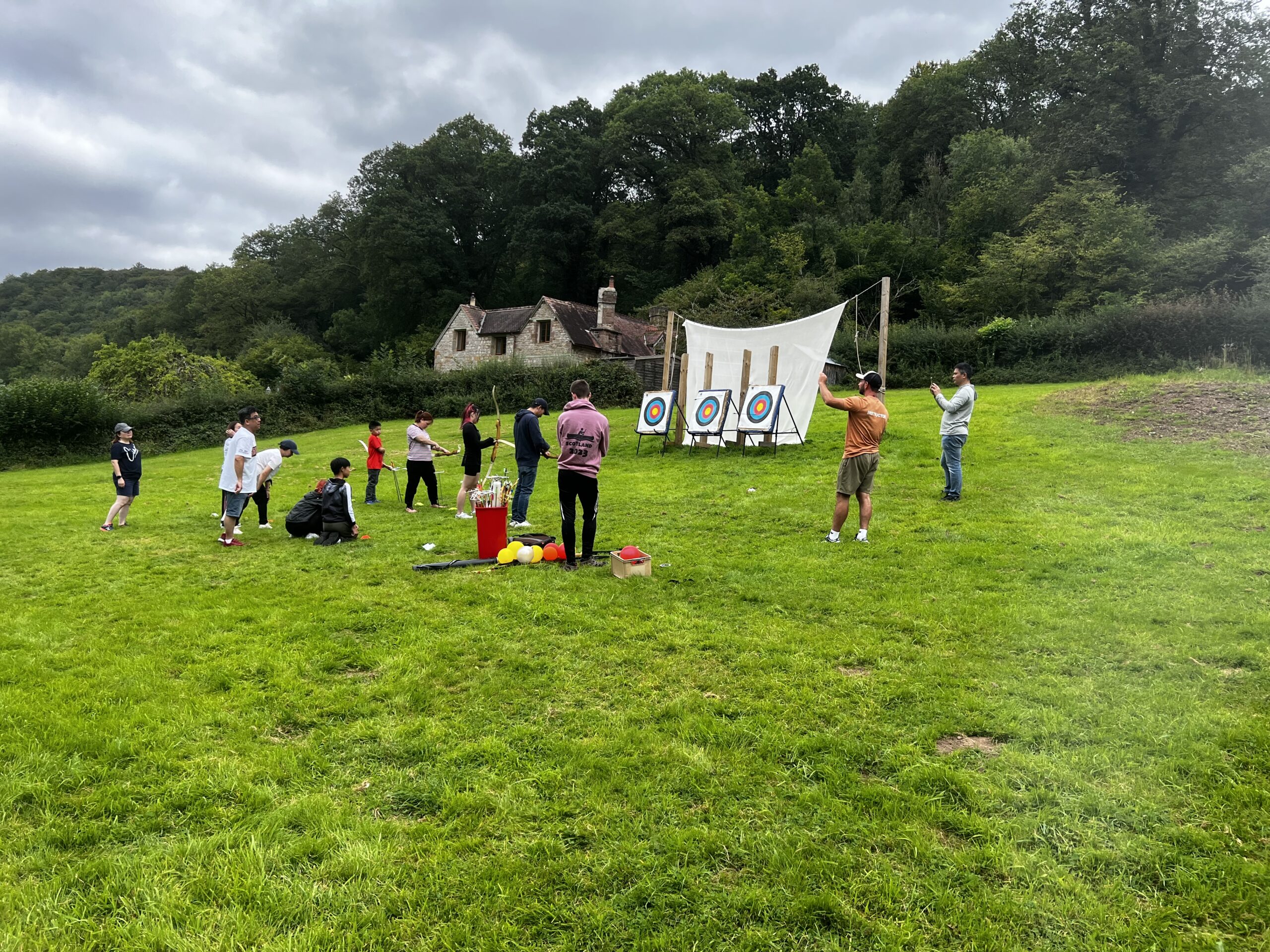 A group of children with instructors on an archery range in a field shooting at targets.