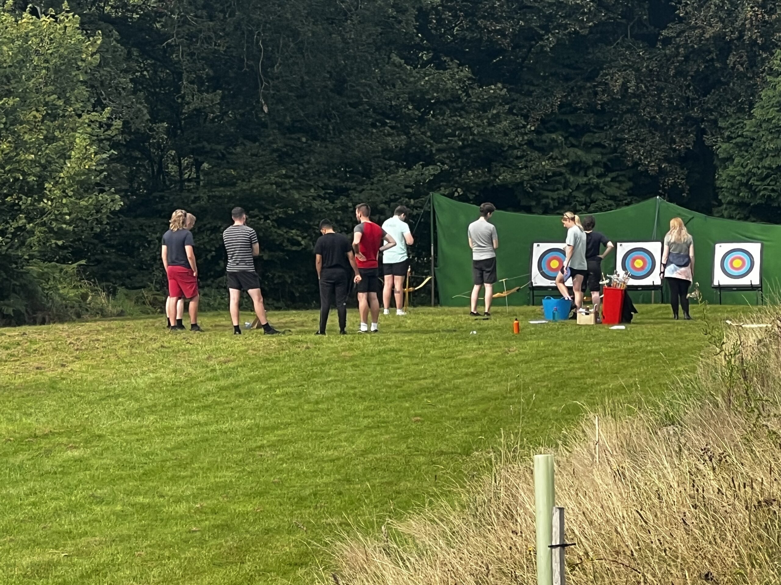 A group of young adults on an archery range in a field lined with trees.
